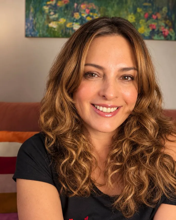 Patricia Casadiego sonriendo, con el cabello rizado suelto, frente a un cuadro de flores